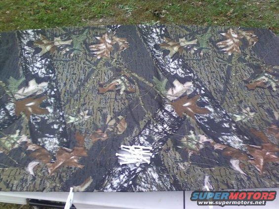 Camouflage fabric with oak leaves pattern laid flat on a surface, with a white plastic object on top