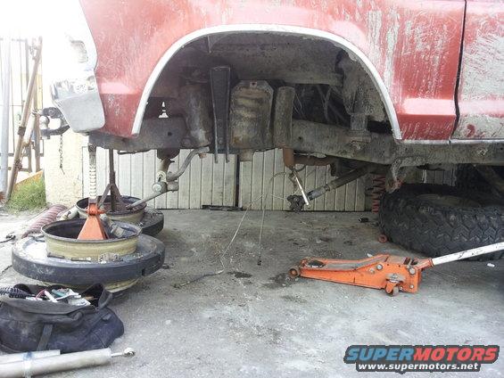 Red 1978 Ford Bronco chassis on jack stands with suspension components visible