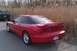 1996 Ford Probe - A red 1996 Ford Probe is parked on the side of the road next to a field of dry grass, with another vehicle visible in the background.