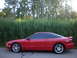 1996 Ford Probe - A red 1996 Ford Probe is parked on the side of the road with tall grass and trees in the background.