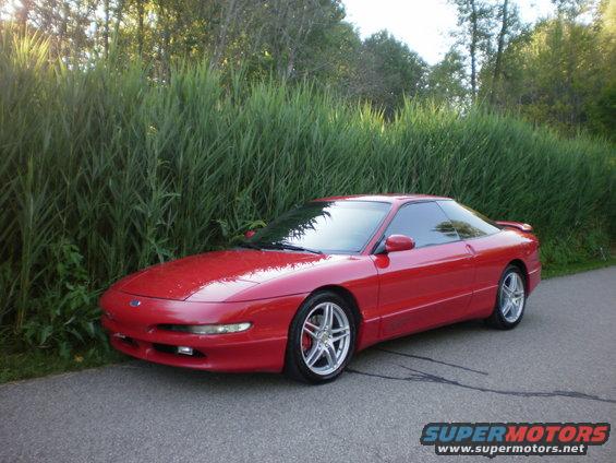 Red 1996 Ford Probe parked on asphalt next to tall grass