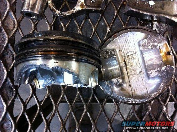 Two severely damaged engine pistons on a metal grate