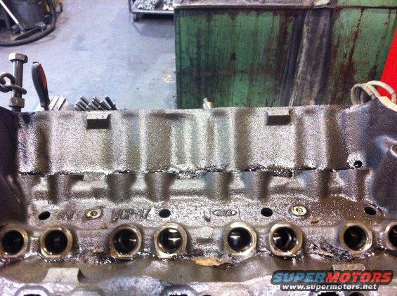 Close-up of an engine block with oil residue. Some text and a Ford logo are visible