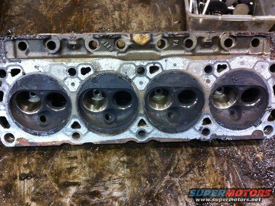 Used engine cylinder head with four combustion chambers visible. Text '8118' is cast into the metal