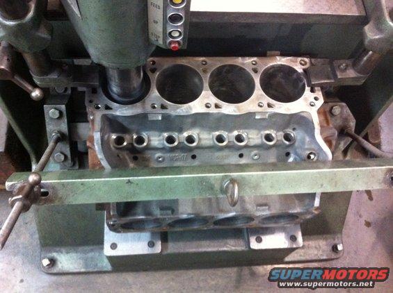 Engine block being machined, showing cylinders and oil passages. Text 'SUPERMOTORS.NET' visible