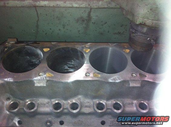 Close-up of engine block cylinders, some showing wear. A machine is visible at the top right