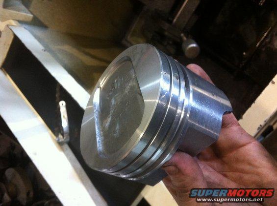Metal piston held in hand, showing machined surfaces and ring grooves