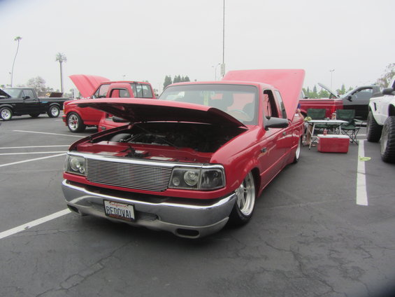 Red Ford Ranger pickup with hood open, parked in a lot with other trucks