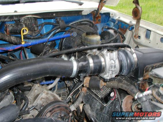 1990 Ford Bronco engine bay with blue firewall, black hoses, and silver throttle body