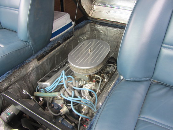 Engine compartment with V8 engine, chrome air cleaner, and blue spark plug wires, viewed between light blue bucket seats