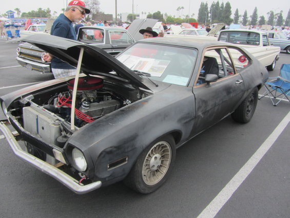 Black Ford Pinto with hood open, showing engine. Other cars and people in background
