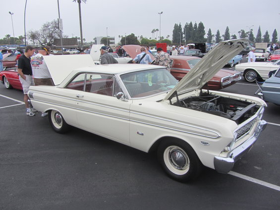 White 1963 Ford Falcon coupe with hood open, parked at an outdoor car show