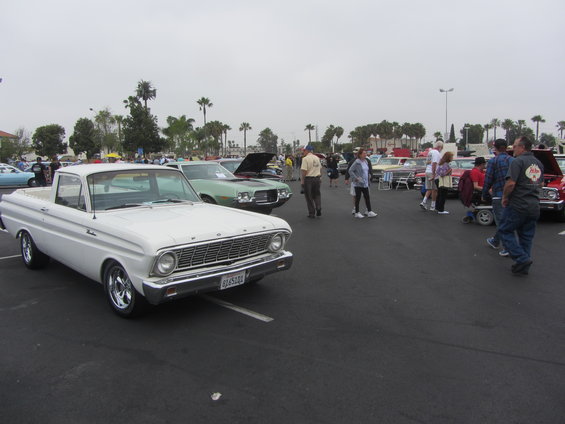 White 1963 Ford Falcon Ranchero parked at a car show with other vehicles and people around