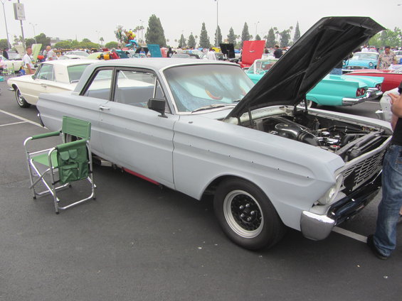 Light gray 1964 Ford Ranchero with hood open, black racing wheels, and a green folding chair beside it