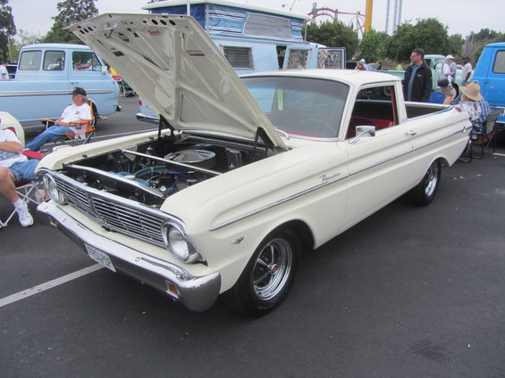 White 1964 Ford Ranchero with hood open, parked next to a blue pickup truck and a camper