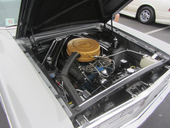 Engine bay with gold air cleaner and a '65 sticker on the windshield