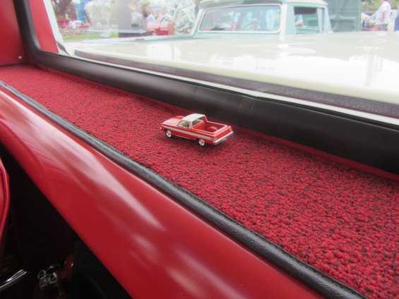 Red and white toy pickup truck on red carpet inside a vehicle