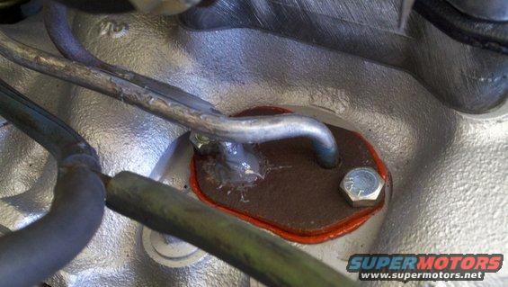 Engine component with a brown gasket secured by a bolt, metal lines nearby