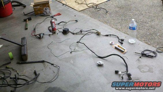 Vehicle wiring harness laid out on concrete floor with tools and a can of spray lubricant