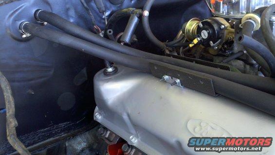 Engine bay with silver valve cover and black hoses. Supermotors.net watermark visible