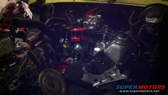 Engine bay with V8 engine, carburetor, and distributor visible. Some parts are red and chrome