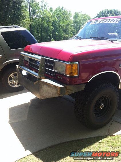 Red pickup truck with a custom metal bumper and an off-road banner on the windshield. Another SUV is parked next to it
