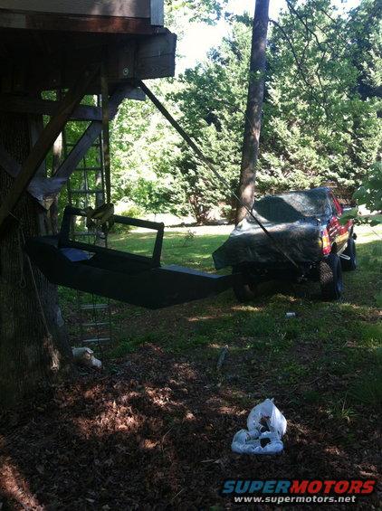Red truck covered by a tarp, parked outdoors next to a treehouse structure