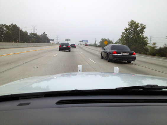 Black sedan driving on a foggy highway, other cars ahead