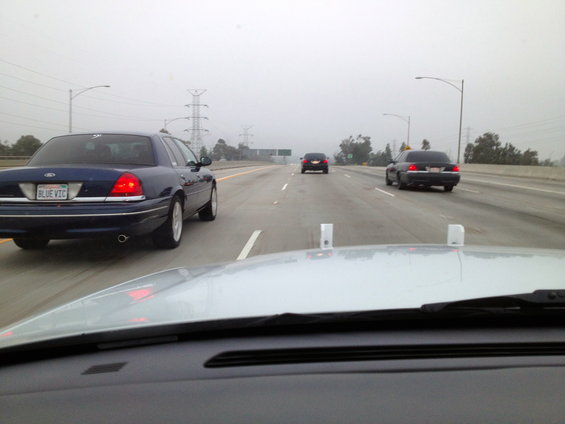 Blue Ford Crown Victoria on highway, rear view. License plate reads 'BLUE VIC'