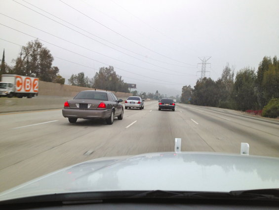 2004 Ford Crown Victoria driving on highway, seen from behind. Other cars and a truck are also on the road