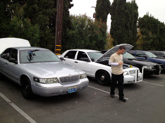 Silver Ford Crown Victoria with hood open, parked in a lot with other similar vehicles