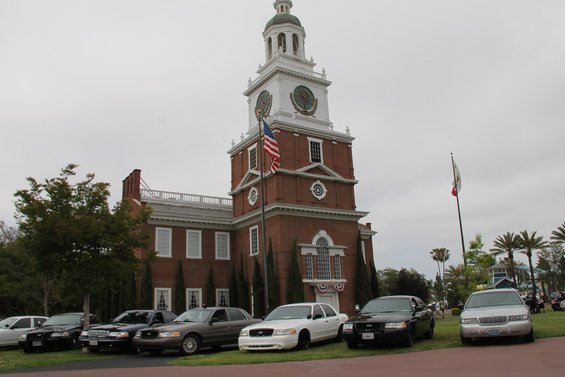 Several Ford Crown Victorias parked in front of a brick building with a clock tower