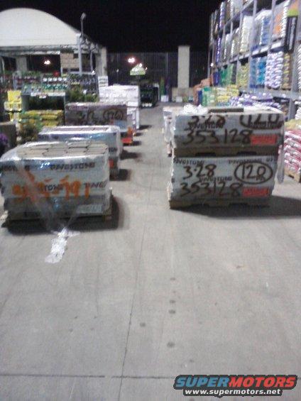 Pallets of paving stones wrapped in plastic sit on wooden pallets in a store aisle at night