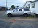 2003 Nissan Frontier - A silver 2003 Nissan Frontier pickup truck with a cap and roof rack is parked on a gravel lot next to a white house.