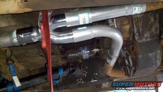 Underside view of a vehicle's exhaust system and transmission, with red and blue straps attached