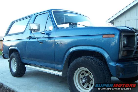 Blue 1980 Ford Bronco with chrome side steps and white wheels parked on a concrete driveway