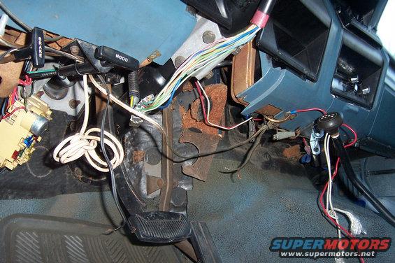 Car interior with exposed wires, pedals, and a gear shift. Shows brake and hood levers