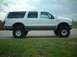2000 Ford Excursion - This lifted Ford Excursion is parked on a paved surface next to a grassy area under a cloudy sky.