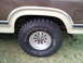 1984 Ford Bronco - Close-up of the rear wheel and fender flare on a brown and tan SUV, a Firestone Destination M/T tire.