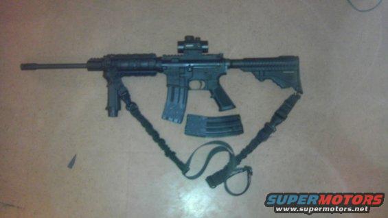 AR-15 style rifle with a red dot sight, foregrip, and two magazines. A sling is attached