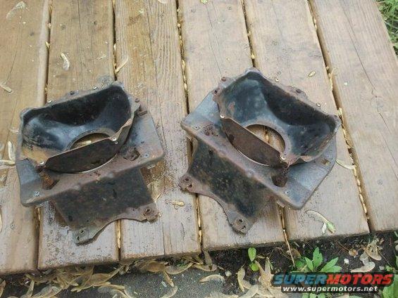 Two rusty, black metal parts with circular openings, resting on wooden planks