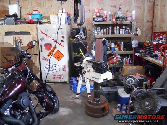 Motorcycle parked in a workshop with a sander, air compressor, and shelves of supplies
