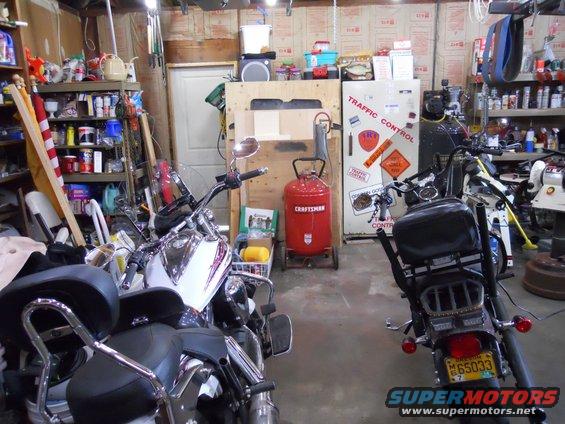 Two motorcycles parked in a cluttered garage with shelves of supplies