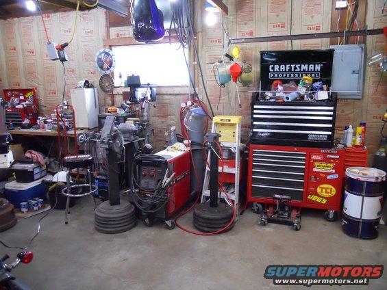 Workshop interior with tools, welding equipment, and tool chests. A motorcycle part is visible in the foreground
