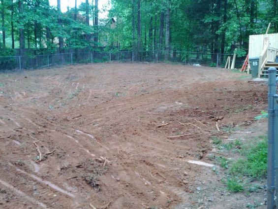 cleared lot with dirt, tree stumps, and a partially built deck in the background