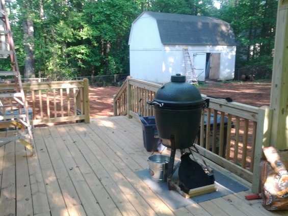 Backyard deck with a large green ceramic grill, a white shed, and trees