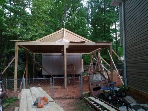 unfinished roof structure, two metal sheds, and a rusty truck cab with a small riding mower on top