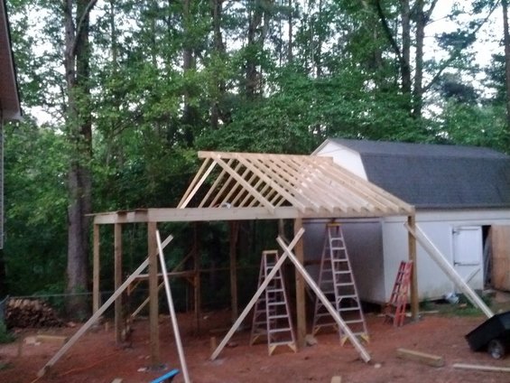 Construction site with unfinished roof framing and a white shed