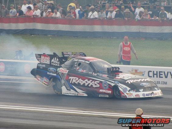 Drag racing car with "Traxxas" livery, emitting smoke from tires, seen from the side