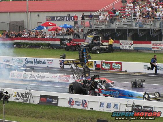 drag race with two dragsters on track, spectators in stands, and pit crew vehicles in background